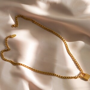 May include: A gold chain necklace with a padlock pendant. The chain is a curb chain style.