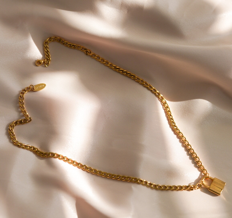 May include: A gold chain necklace with a padlock pendant. The chain is a curb chain style.