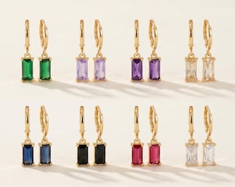 May include: Eight pairs of gold-tone hoop earrings, each featuring a rectangular baguette-cut gemstone pendant. The stones are available in green, light purple, dark purple, clear, blue, black, red, and white, all set in polished gold-tone metal.