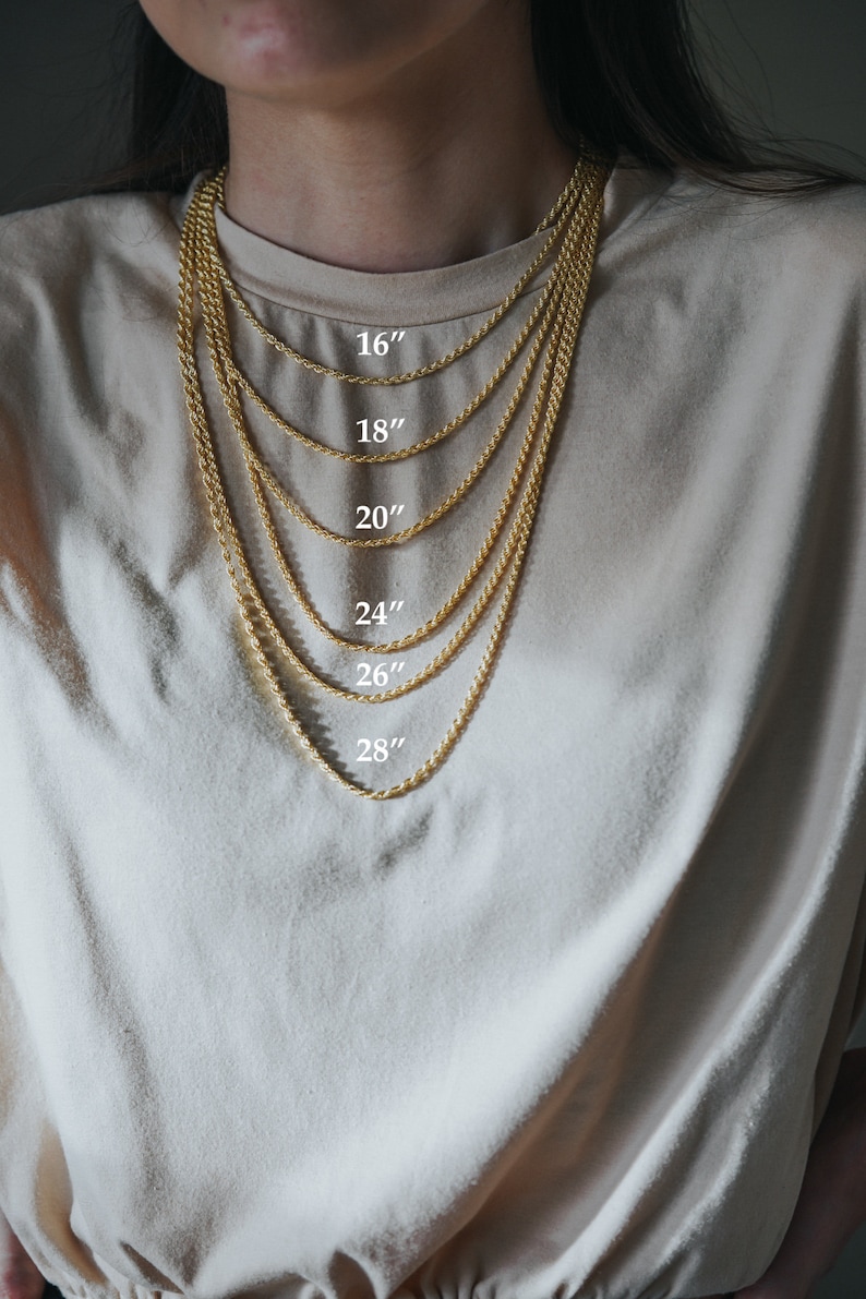 May include: A gold rope chain necklace is shown in different lengths, from 16 inches to 28 inches. The necklace is worn by a person with a light brown shirt.