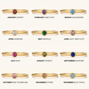 May include: A collection of gold-colored rings, each featuring a different gemstone. The rings are labeled with the months of the year and corresponding birthstones: garnet, amethyst, aquamarine, diamond, emerald, light amethyst, ruby, peridot, sapphire, pink tourmaline, citrine, and blue topaz.