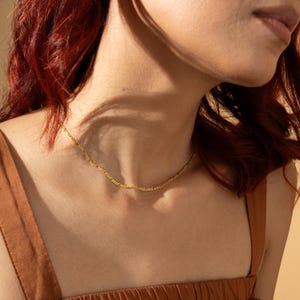 Puede incluir: Un delicado collar de cadena dorada con un dise&ntilde;o sutil y texturizado. El collar se lleva alrededor del cuello. La persona lleva un top marr&oacute;n. El fondo es de un tono c&aacute;lido y neutro. La cadena mide unos 40 cm.
