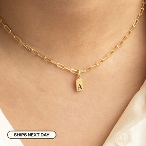 May include: A gold chain necklace with a small gold tag pendant that has the letter "A" engraved on it.