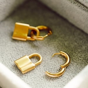 May include: Two gold lock and key earrings in a gray velvet jewelry box.