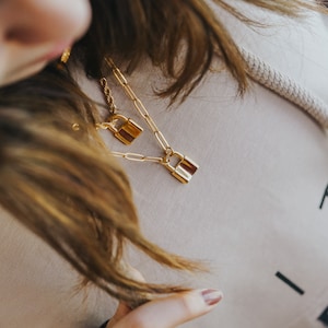May include: A gold chain necklace with two padlock pendants. The necklace is layered and the padlocks are different sizes.