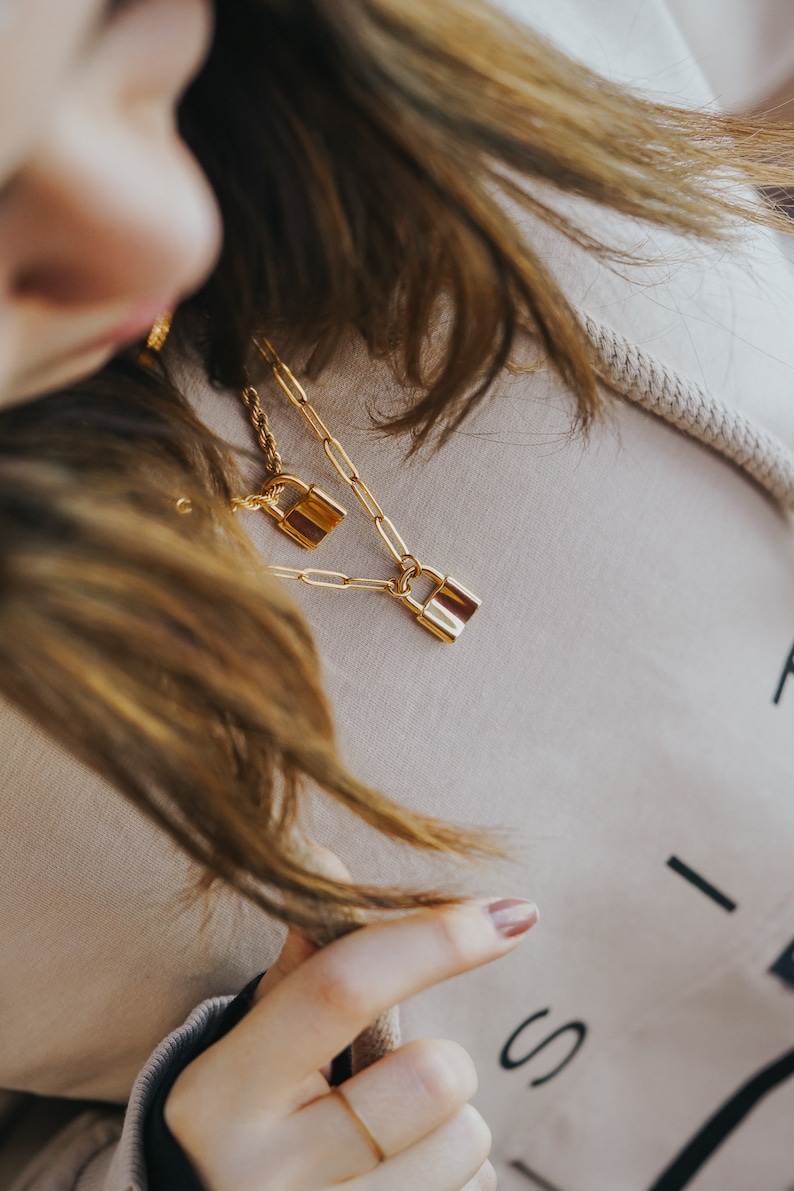 May include: A gold chain necklace with two padlock pendants. The necklace is layered and the padlocks are different sizes.
