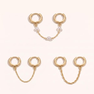 May include: Three pairs of gold-toned hoop earrings connected by chains. One pair features a delicate gold chain with three small white pearls. The second pair has a simple thin gold chain. The third pair includes a twisted gold chain design.