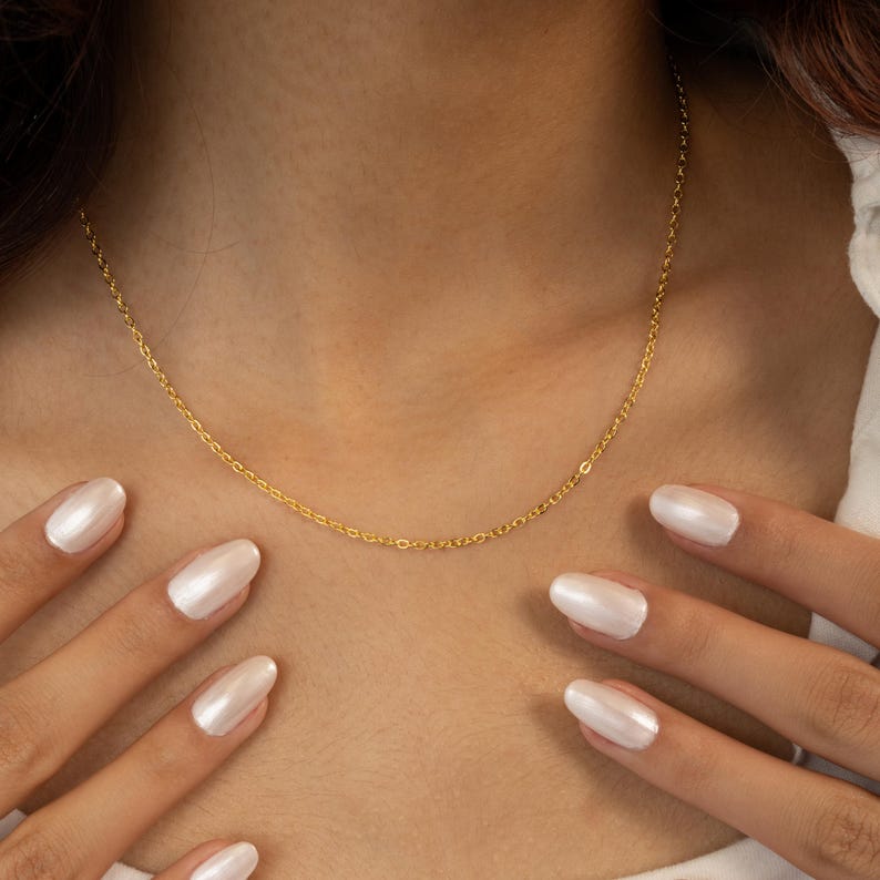Op de afbeelding: Een gouden kettingketting die om de nek van een persoon wordt gedragen. De ketting is dun en delicaat.