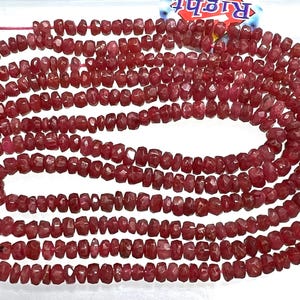 May include: Multiple strands of small, faceted, reddish-pink gemstone beads. The beads are uniform in size and strung together. The beads are a deep, rich colour, and the facets catch the light, creating a layered effect.