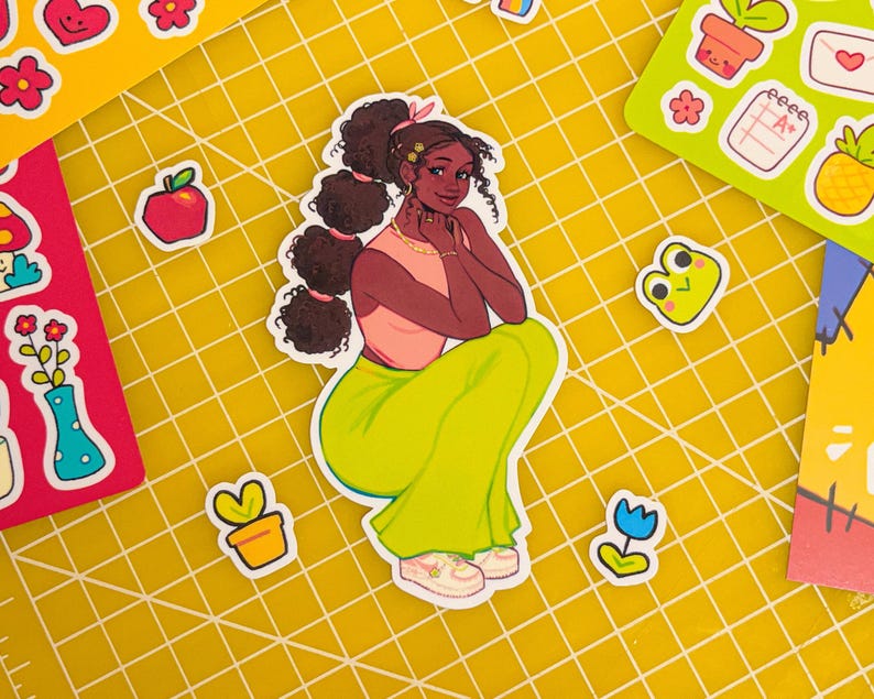 May include: A sticker of a cartoon woman with brown hair, wearing a pink shirt and green pants. She is sitting with her legs crossed and has a flower in her hair.