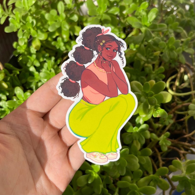 May include: A sticker featuring a cartoon illustration of a woman with brown hair in a ponytail, wearing a pink top and yellow pants. She is sitting with her hands on her chin and looking at the viewer.