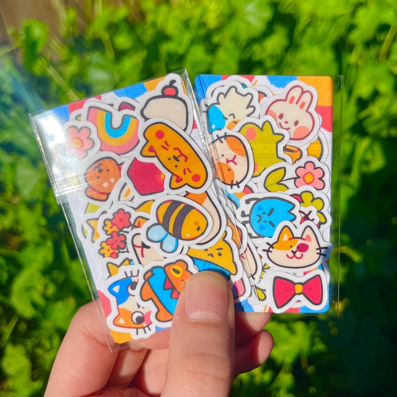 May include: A clear plastic bag filled with colourful stickers featuring cartoon animals, flowers, and geometric shapes. The stickers are on a white background.