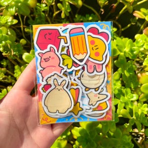 May include: A sheet of colorful stickers featuring various cartoon characters, including a pig, a bunny, a pencil, and a heart. The stickers are on a white background with a colorful border.