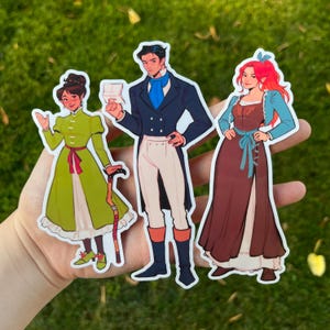 May include: Three die-cut stickers featuring stylized illustrations of characters in period clothing. The characters are a woman in a green dress, a man in a blue coat, and a woman in a brown dress. The stickers are held in a hand against a green background.