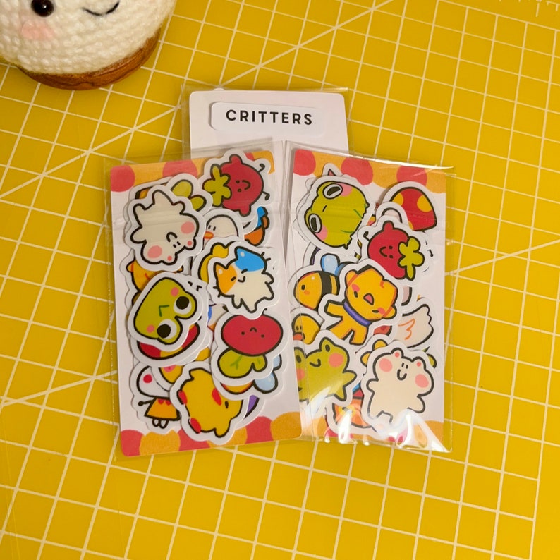 May include: Two packs of stickers featuring cute cartoon critters. The stickers are on a white background with a yellow and red border. The text "CRITTERS" is printed on the top of the packs.