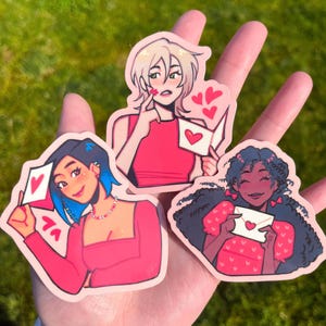 May include: Three illustrated stickers featuring women with pink and red clothing and hearts. The women are holding cards with hearts on them.