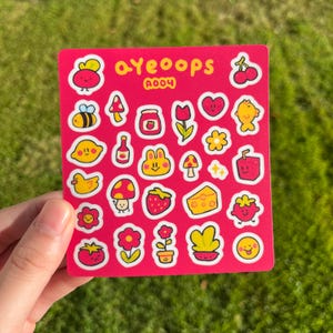 May include: A sheet of pink stickers with various cute illustrations, including a bee, lemon, mushroom, strawberry, and flowers. The text "ayeoops" and "A004" are printed in yellow.