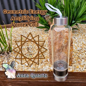 May include: A clear glass bottle with a silver lid and a silver base. The bottle contains a copper coil and a clear crystal. The bottle is surrounded by small rocks and a wooden surface. The text "Geometric Energy Amplifying Vortex Coil" and "Aura Quartz" is visible in the image.