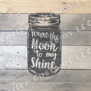 May include: A mason jar with the text "You're the Moon to my Shine" on a wooden background.