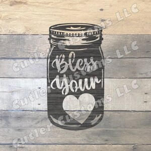 May include: A dark grey mason jar design featuring the words "Bless your heart" and a heart shape. The jar is set against a rustic, light brown and grey wooden background.