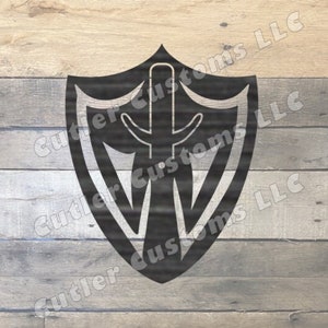 Könnte beinhalten: Schwarzer Metallschild mit einem stilisierten Design aus Schwert und Flügeln. Der Schild befindet sich auf einem Holzgrund.