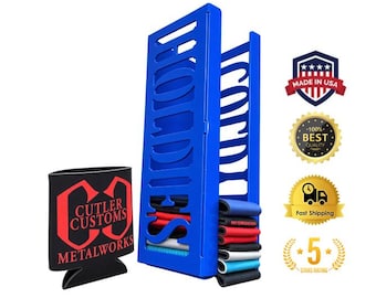 May include: A blue vertical metal storage rack with the word HOODIES cut out of the side, holding a stack of folded fabric sleeves. Next to it is a black foam beverage insulator with the red text CUTLER CUSTOMS METALWORKS printed on it.