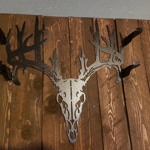 May include: A metal deer skull wall mount with antlers. The skull is silver and the antlers are black. The mount is attached to a wooden wall.
