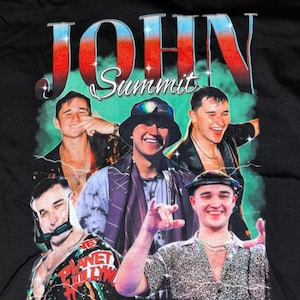 May include: Black t-shirt with a graphic print of a band called "John Summit". The graphic features four men in a retro style with a green, blue, and red color scheme.