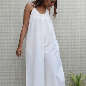 May include: A white sleeveless jumpsuit with a scoop neck and wide legs. The jumpsuit is made of a lightweight fabric and has a relaxed fit.