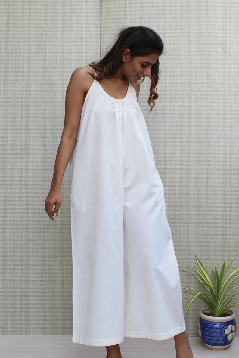 May include: A white sleeveless jumpsuit with a scoop neck and wide legs. The jumpsuit is made of a lightweight fabric and has a relaxed fit.