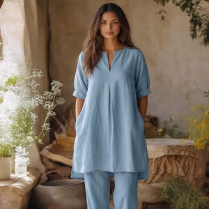 May include: A light blue linen tunic and matching pants set. The tunic features a V-neckline, short sleeves, and front pockets. The pants are a straight-leg style. The outfit is made of a soft, flowing fabric, perfect for warm weather.