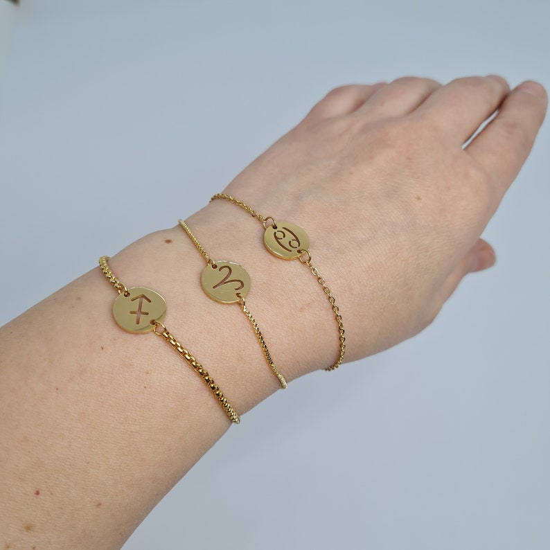 May include: Three gold chain bracelets with zodiac signs. The bracelets feature a Sagittarius, Aries, and Cancer symbol.