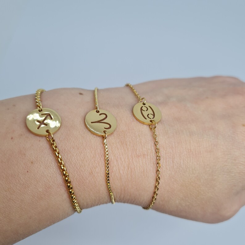 May include: Three gold chain bracelets with zodiac signs. The bracelets feature a Sagittarius, a Gemini, and a Cancer symbol.