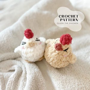 May include: Two crocheted chicken toys, one white and one tan, with red comb details. The toys have black eyes and pink cheeks. The text "CROCHET PATTERN" and "CLUCK THE CHICKEN" is in a white cloud-shaped graphic.