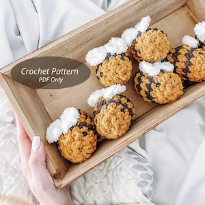 May include: A wooden box filled with crocheted bee toys. The bees are yellow and black with white accents. The box has a sign that says "Crochet Pattern PDF Only".