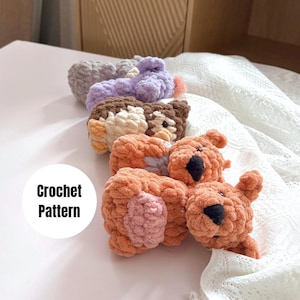 May include: A row of four small, plush, handmade crochet animal figures in shades of gray, purple, brown, and orange, featuring black stitched noses and eyes. A white circular graphic with the black text Crochet Pattern is visible.