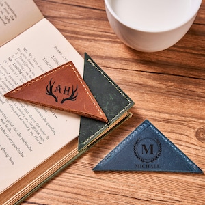 Peut inclure: Deux marque-pages en cuir avec des initiales et des motifs personnalisés. Le premier marque-page est brun avec un motif d'antenne de cerf et les initiales "AH". Le deuxième marque-page est bleu avec un motif de laurier et les initiales "M" avec le nom "MICHAEL" en dessous.