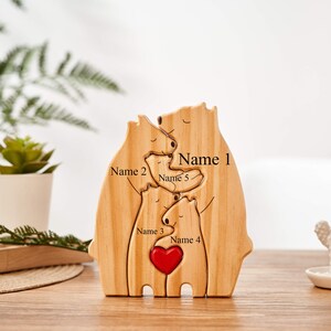 Puede incluir: Escultura de madera de una familia de osos con un coraz&oacute;n rojo en el centro. Los osos est&aacute;n dispuestos en un abrazo, con los nombres "Nombre 1", "Nombre 2", "Nombre 3", "Nombre 4" y "Nombre 5" inscritos en la madera.