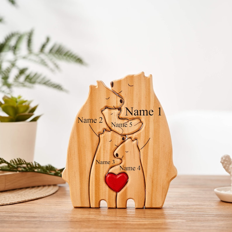 Puede incluir: Escultura de madera de una familia de osos con un coraz&oacute;n rojo en el centro. Los osos est&aacute;n dispuestos en un abrazo, con los nombres "Nombre 1", "Nombre 2", "Nombre 3", "Nombre 4" y "Nombre 5" inscritos en la madera.