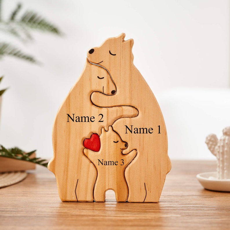 Puede incluir: Puzzle de madera de una familia de osos con tres osos, dos osos m&aacute;s grandes abrazando a un oso m&aacute;s peque&ntilde;o. Los osos tienen un coraz&oacute;n rojo entre ellos. El rompecabezas est&aacute; personalizado con los nombres "Nombre 1", "Nombre 2" y "Nombre 3".