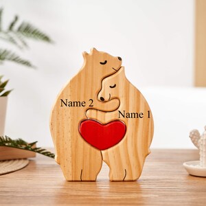 Puede incluir: Corte de madera de dos osos abraz&aacute;ndose con un coraz&oacute;n rojo en el centro. Los osos est&aacute;n personalizados con los nombres "Nombre 1" y "Nombre 2".
