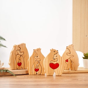 Puede incluir: Cinco figuritas de madera de una familia de osos, cada una con un coraz&oacute;n rojo, de pie sobre una superficie de madera. Los osos est&aacute;n tallados en una pose de abrazo, simbolizando el amor y la familia.