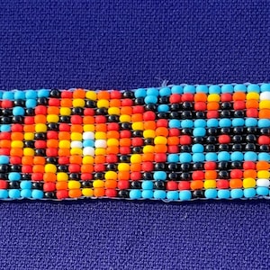 May include: A turquoise beaded bracelet with a colorful geometric pattern in the center. The bracelet has silver metal clasps on each end.