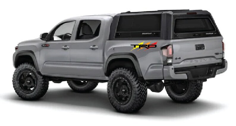 K&ouml;nnte beinhalten: Ein silberner Pick-up mit einer schwarzen Pritschenabdeckung und einem "TRD"-Aufkleber an der Seite. Der LKW hat schwarze R&auml;der und Reifen.