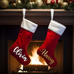 Puede incluir: Dos calcetines de Navidad rojos con puños blancos colgando sobre una chimenea. El calcetín de la izquierda tiene el nombre "Olivia" escrito en blanco en la parte delantera. El calcetín de la derecha tiene el nombre "Harry" escrito en dorado en la parte delantera.