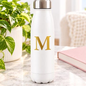 Peut inclure: Une bouteille d'eau en acier inoxydable blanc avec un bouchon à vis en argent métallique. L'avant de la bouteille présente une grande lettre capitale M dorée centrée dans une police serif. La bouteille a une finition mate et une base arrondie.