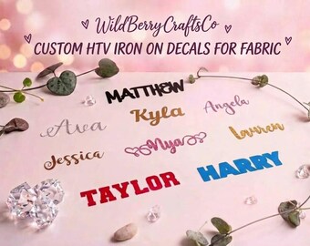 May include: Custom HTV iron-on decals for fabric by WildBerryCraftsCo featuring various names in different fonts and colors, including black, gold, silver, pink, red, and blue glitter finishes, displayed on a light pink surface.