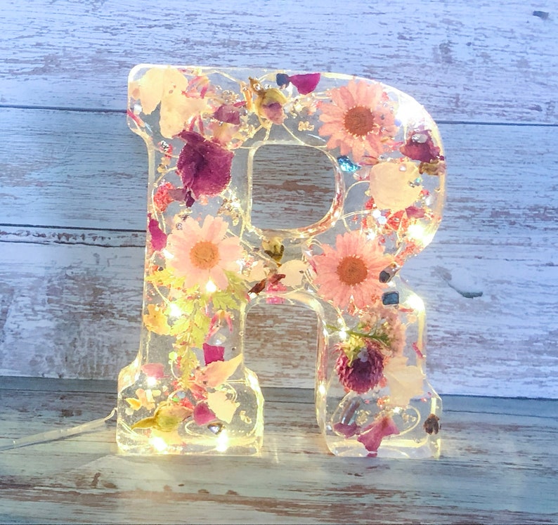 Handmade Clear like Glass Personalized Letters. A to Z available. Filled with dried flowers, glitters, flakes, and crystal chips. Comes in Pink, Blue, Purple, Orange, Red, Yellow or White flowers. Includes battery fairy lights incased in the letter.
