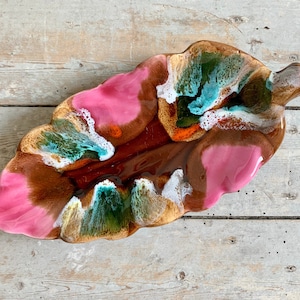 May include: A leaf-shaped ceramic dish with a glossy finish. The dish has a blend of pink, brown, green, and white, creating a unique, artistic appearance. The leaf design adds a touch of nature-inspired decor. A decorative item.