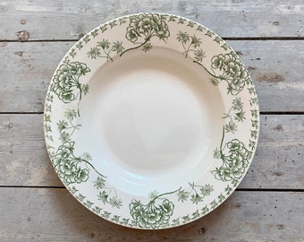 May include: White ceramic serving bowl with a green floral pattern around the rim. The bowl has a wide, shallow design and sits on a weathered wooden surface. The floral design features clusters of flowers and leaves.